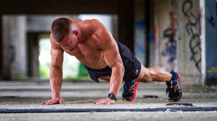 Shirtless caucasian man doing push-ups in an urban setting, showcasing strength and fitness.